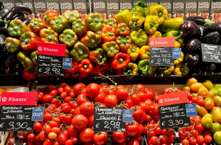 Red, yellow and green peppers above a display of tomatoes and aubergines.